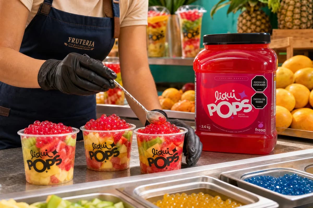 Vasos de fruta picada coronados con perlas explosivas LiquiPops rojas junto al tarro sabor fresa en una frutería