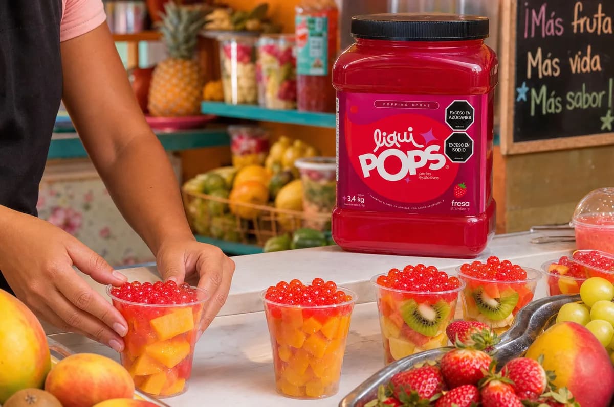 Vasos de fruta con mango y kiwi coronados con perlas explosivas LiquiPops rojas junto al tarro sabor fresa en una frutería