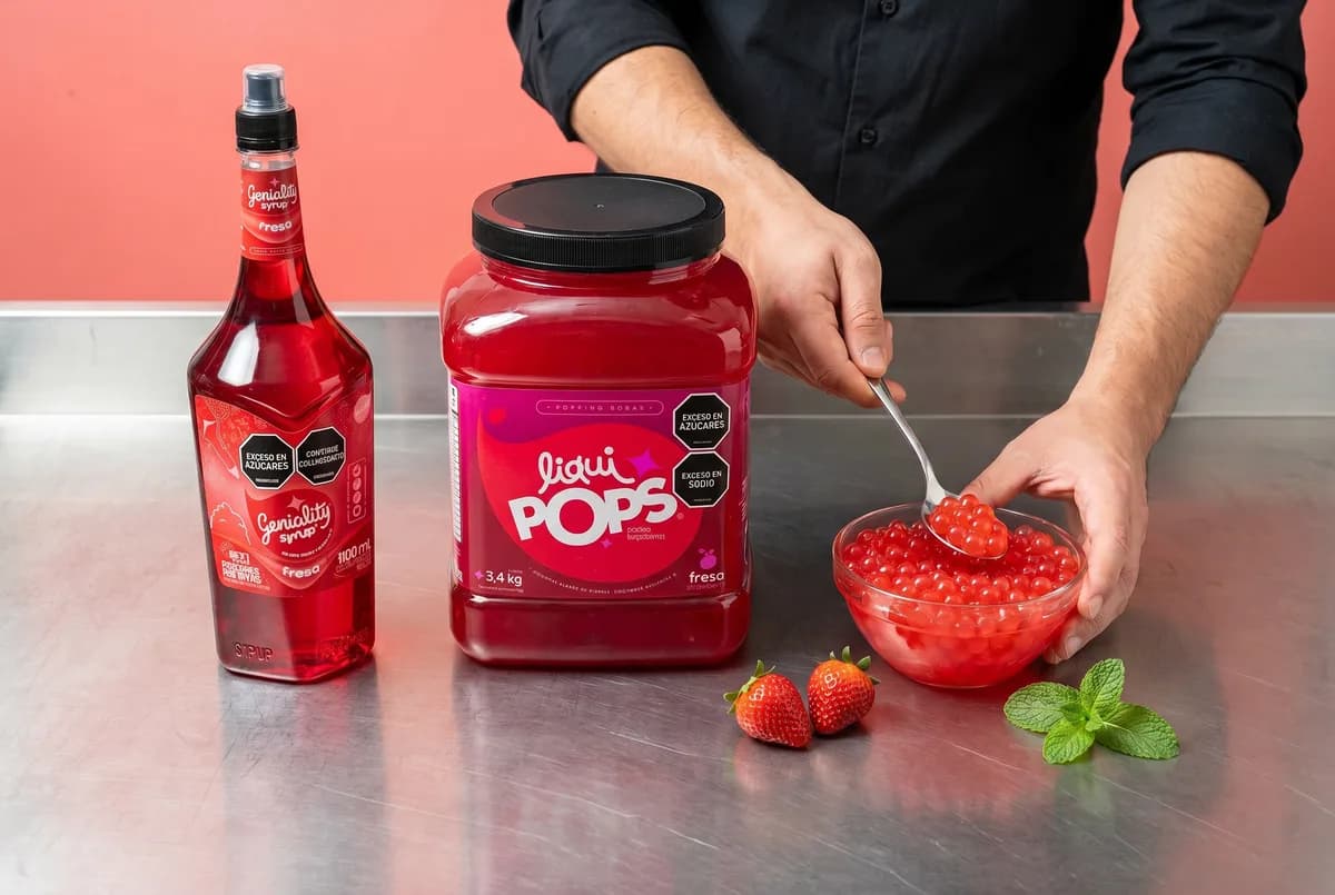 Tarro de perlas explosivas de fresa LiquiPops y sirope Geniality fresa servidos con cuchara en cocina de bar — insumos para emprender