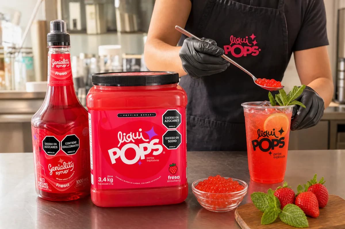 Barista preparando una soda de fresa con perlas explosivas LiquiPops, sirope Geniality de fresa, tina de fresa de 3,4 kg y fresas frescas sobre mesa de acero