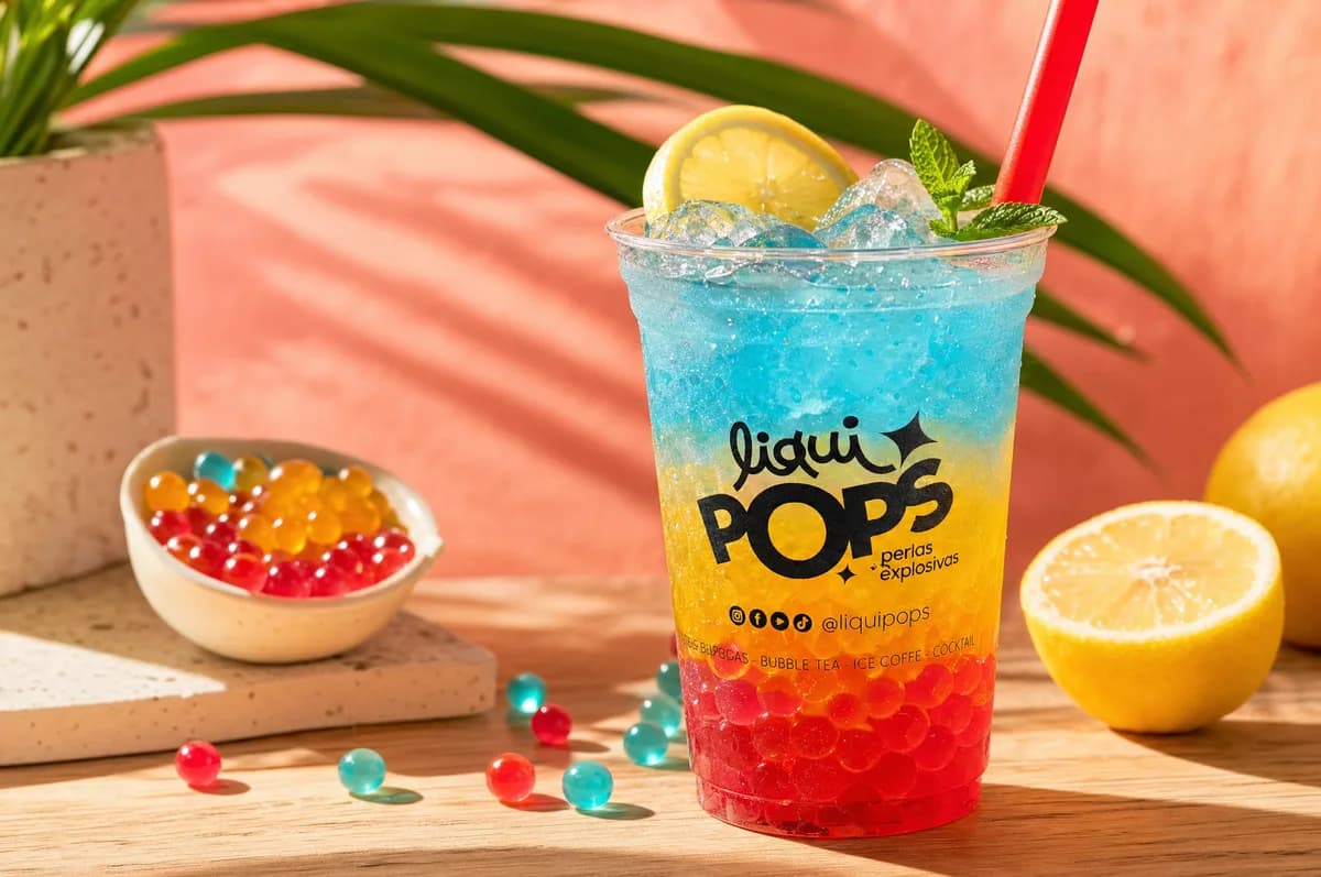 Soda loca en capas azul, amarillo y rojo con perlas explosivas LiquiPops, hielo, limón y hierbabuena en vaso de marca