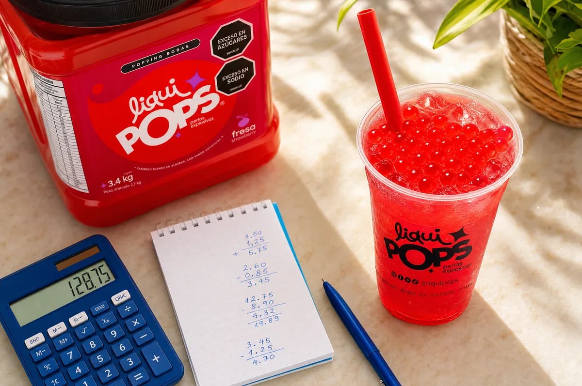Soda loca de fresa con perlas explosivas LiquiPops servida en vaso, junto al tarro de 3,4 kg y una calculadora para costear