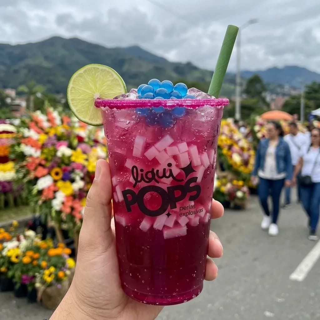 Soda loca fucsia con perlas explosivas azules LiquiPops — borde de chamoy, limón y trozos de coco, feria de las flores de fondo