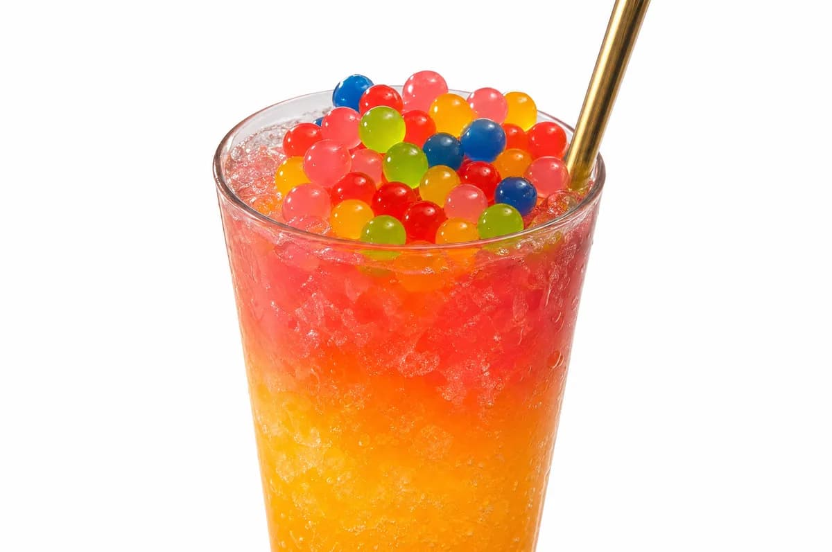 Vaso alto de soda loca degradada roja y naranja con corona de perlas explosivas multicolor LiquiPops y pitillo dorado, sobre fondo blanco
