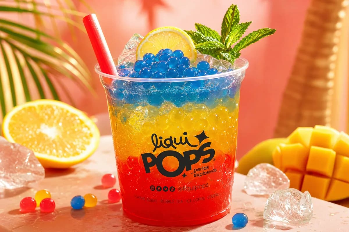 Soda loca tricolor con perlas explosivas azul mora, amarilla y roja LiquiPops sobre hielo — bebida en escena tropical
