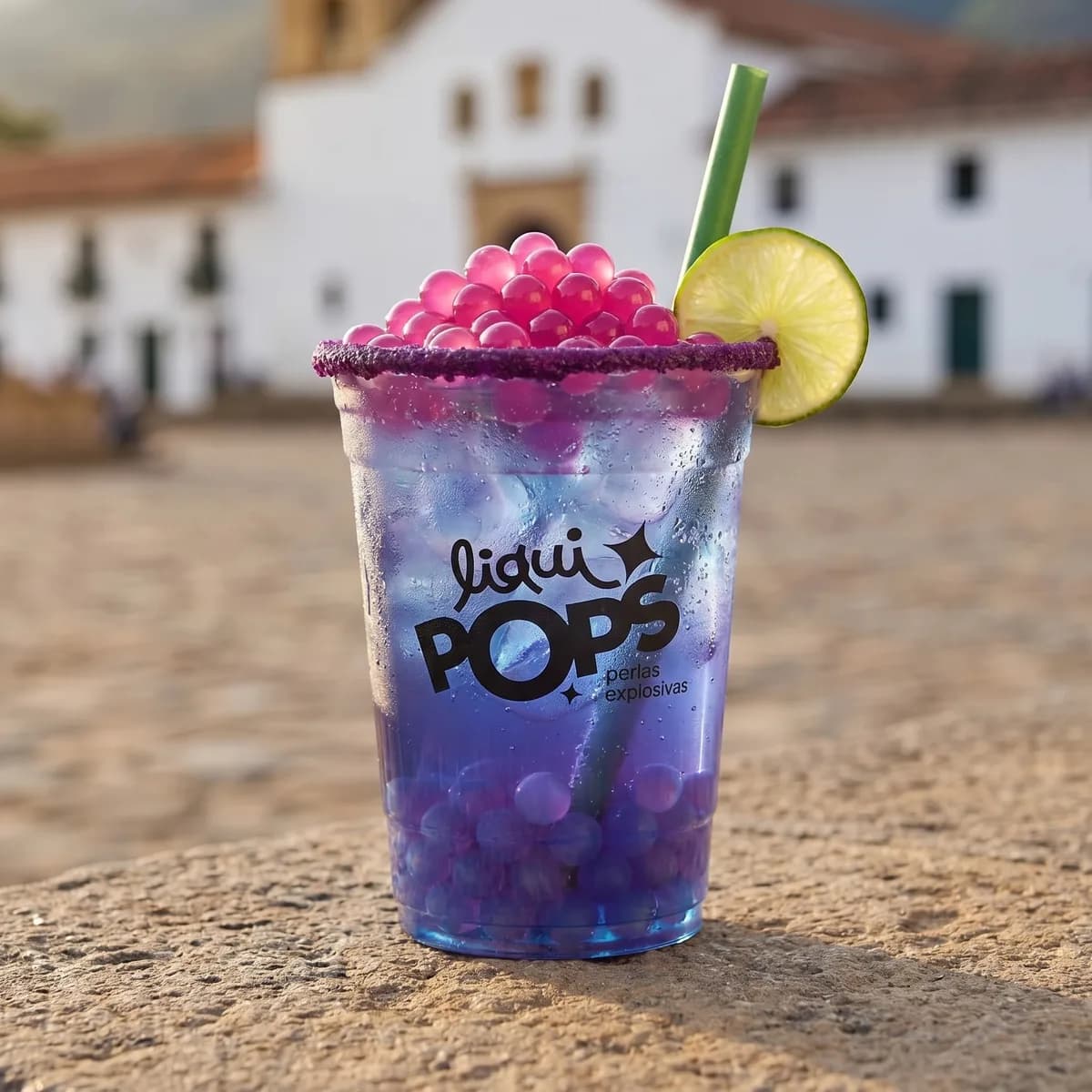 Soda loca morada con perlas explosivas LiquiPops sabor frambuesa, escarcha de uva y rodaja de limon — plaza colonial colombiana al fondo