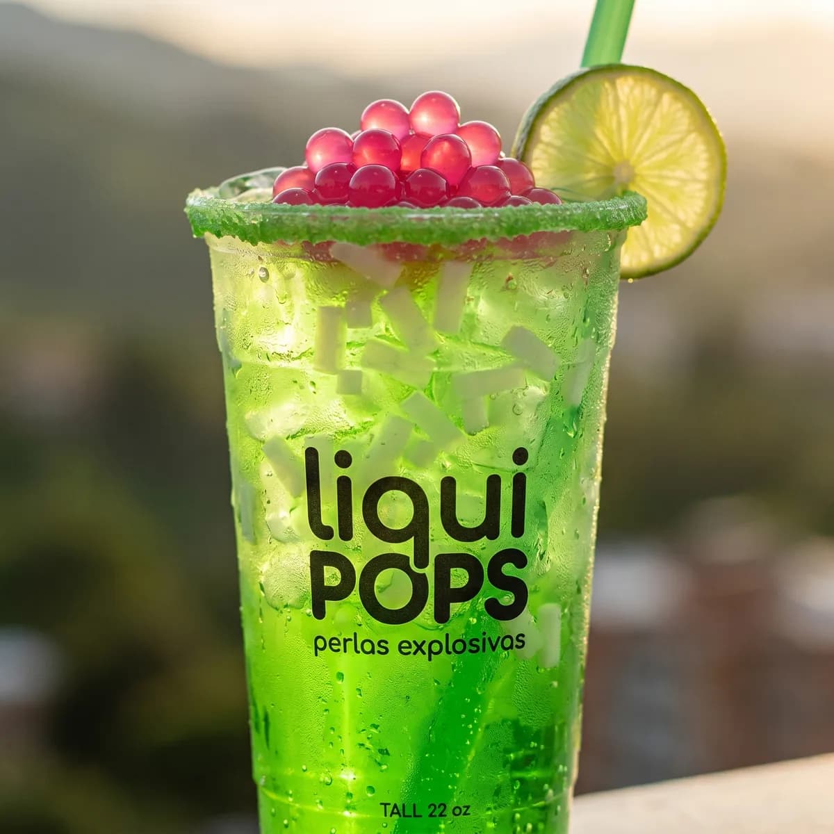 Soda loca verde manzana con perlas explosivas rojas LiquiPops — vaso tall 22 oz escarchado con rodaja de lima y vista a la montaña