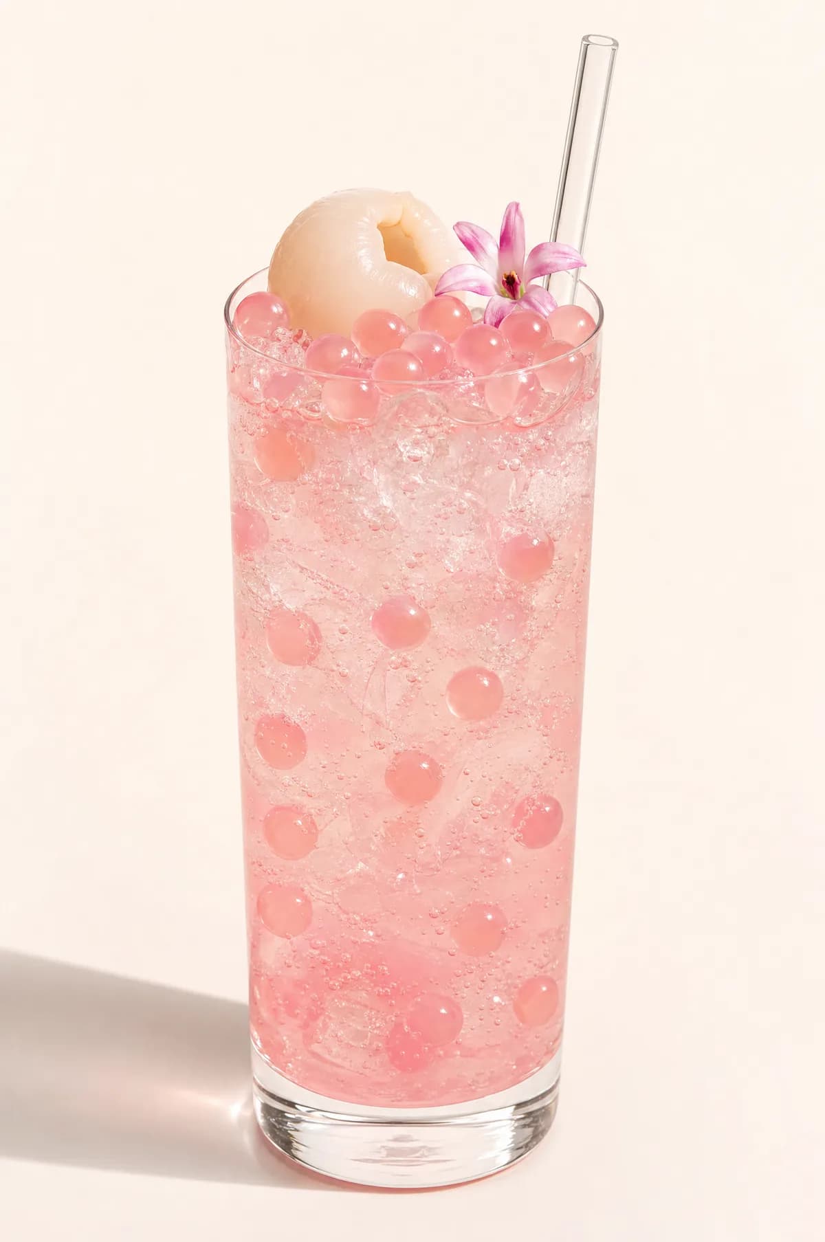 Soda rosada de lychee con perlas explosivas LiquiPops — vaso alto con lychee y flor de garnish