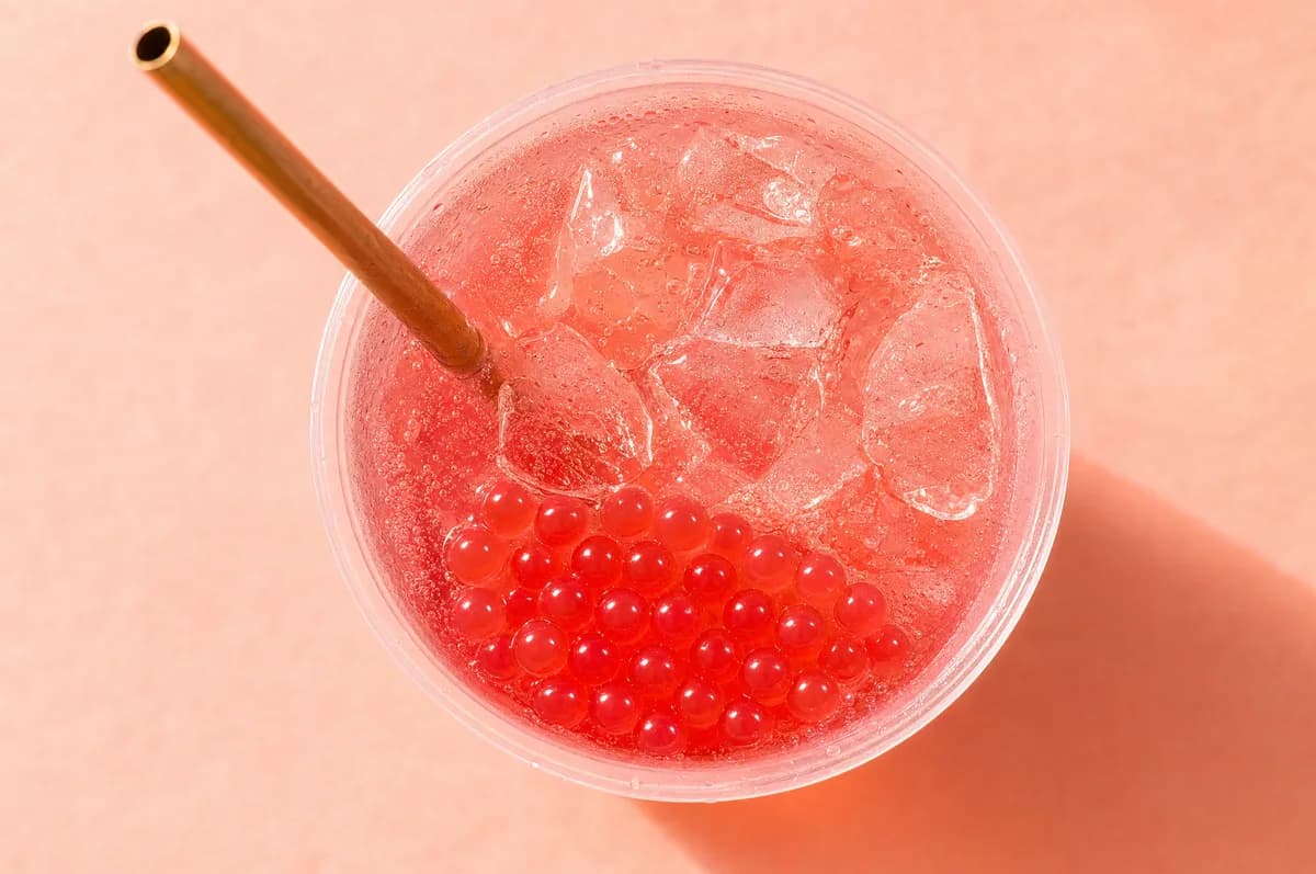 Soda roja de frutos rojos con hielo y perlas explosivas LiquiPops vista desde arriba — vaso con pitillo metálico