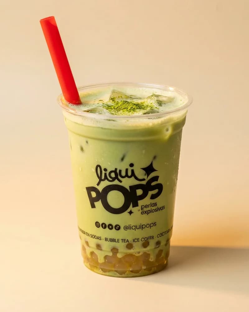 Vaso de bubble tea de matcha con perlas explosivas LiquiPops en el fondo — pitillo rojo sobre fondo beige
