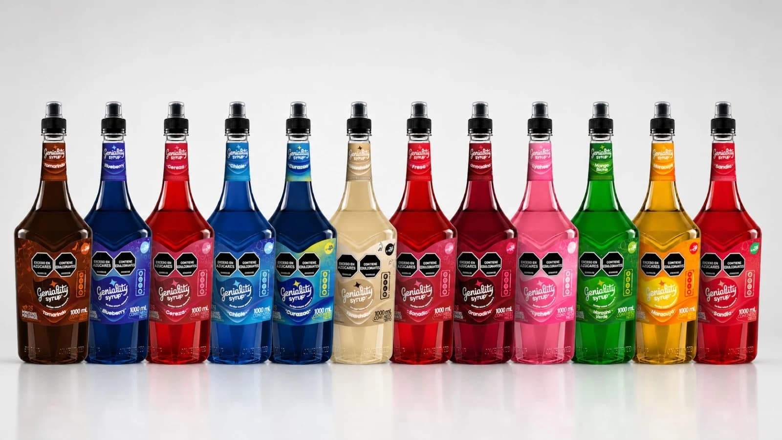 Línea completa Geniality — 12 botellas de sirope extraconcentrado (Tamarindo, Blueberry, Cereza, Chicle, Curazao, Fresa, Granadina, Lychee, Manzana Verde, Mango Biche, Maracuyá, Sandía) más jarabe escarchador alineadas — fabricación Medellín, INVIMA NSA:0019786-2025