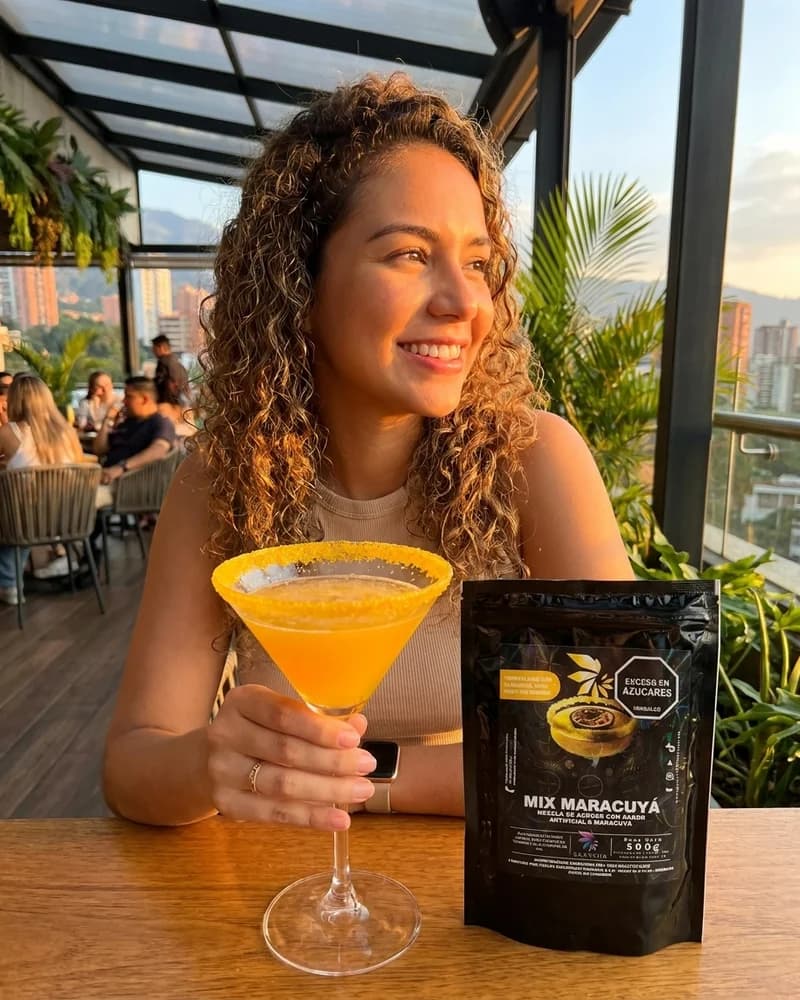 Mujer en terraza de Medellin con copa de maracuya escarchada Skarcha y perlas explosivas LiquiPops junto a la bolsa mix maracuya by LiquiPOPS