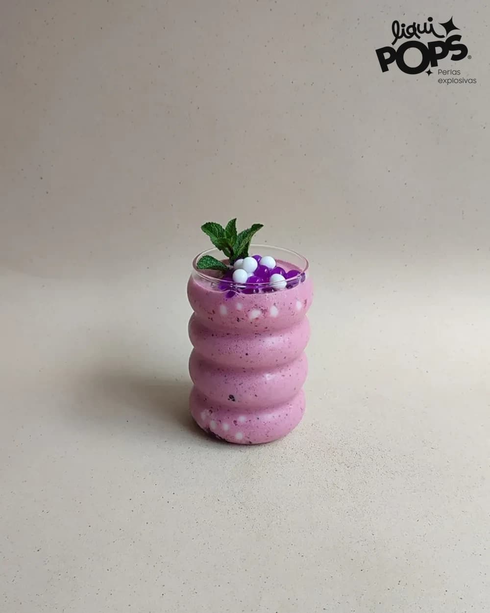 Smoothie de frutos rojos con perlas explosivas moradas LiquiPops y hierbabuena en vaso ondulado