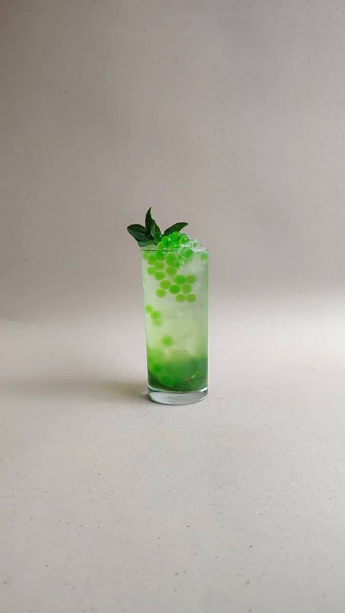 Soda de manzana verde con perlas explosivas verdes LiquiPops y hierbabuena sobre fondo beige
