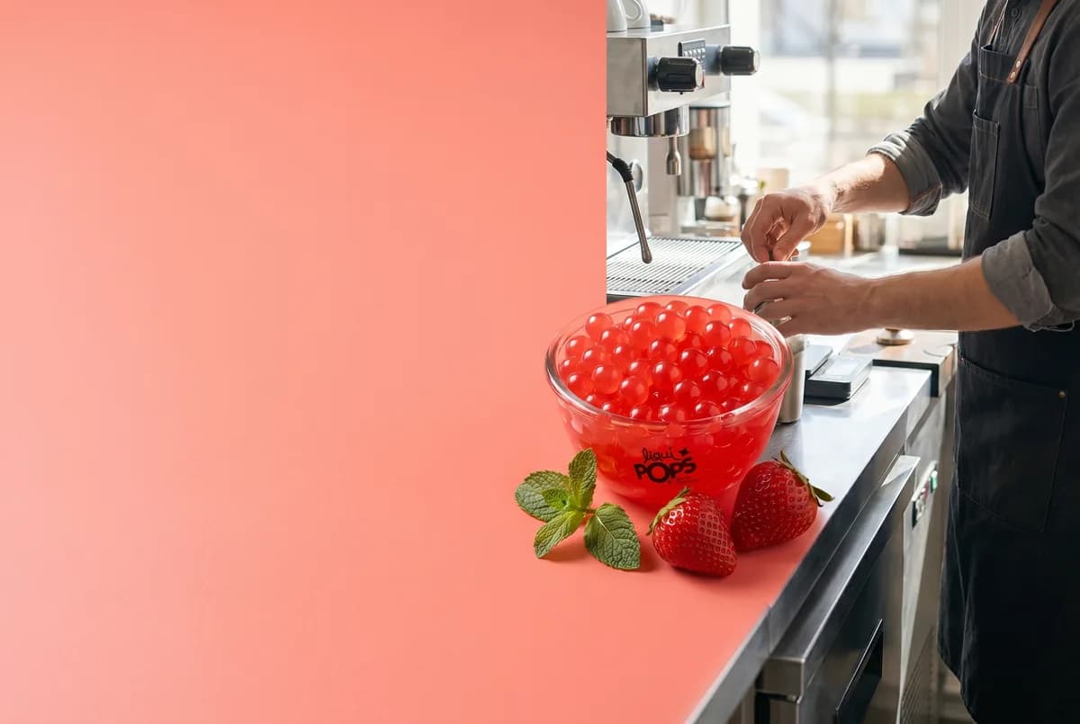 Bowl de perlas explosivas LiquiPops sabor fresa en barra de cafetería con barista al fondo — fresas y menta frescas, contexto profesional