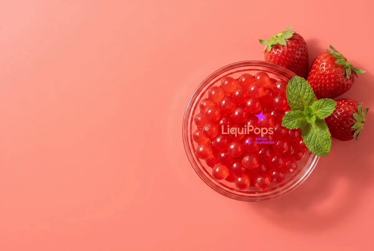 Bowl de perlas explosivas de fresa con fresas y hojas de menta sobre fondo coral — perlas explosivas LiquiPops para tus bebidas