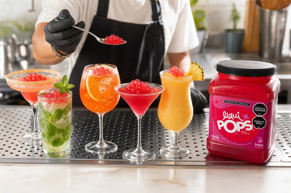 Cinco cócteles surtidos coronados con perlas explosivas rojas LiquiPops mientras un bartender añade una cucharada