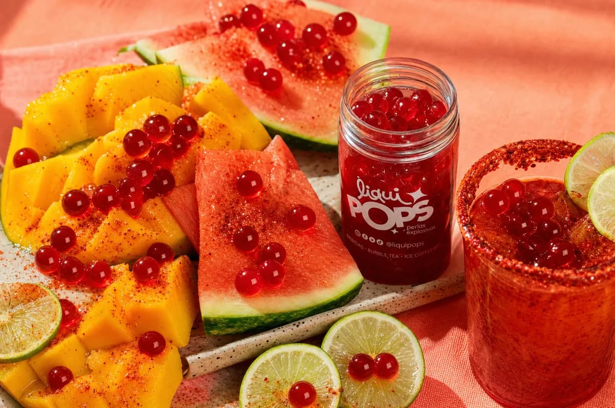 Frasco de perlas explosivas LiquiPops con mango, sandía y lima sobre tabla de madera — bodegón de ingredientes