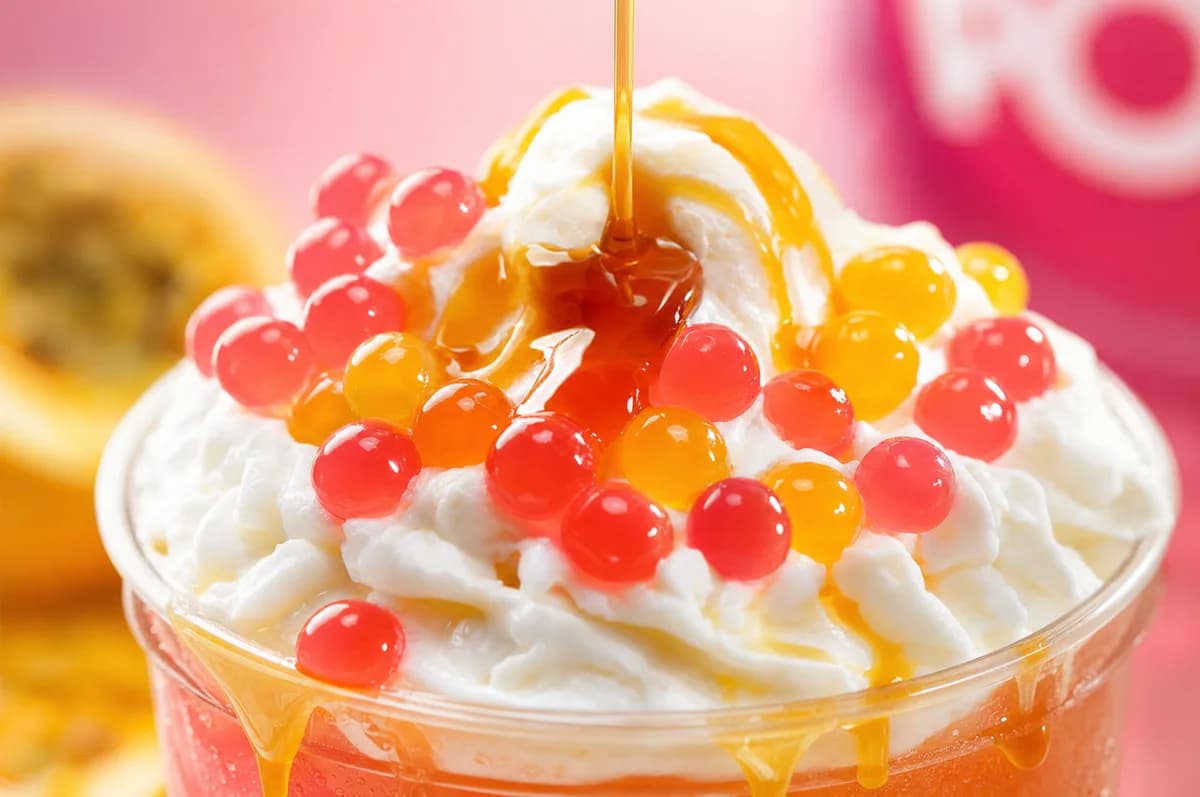 Granizado de maracuyá coronado con crema batida, sirope y perlas explosivas rojas y amarillas LiquiPops — primer plano