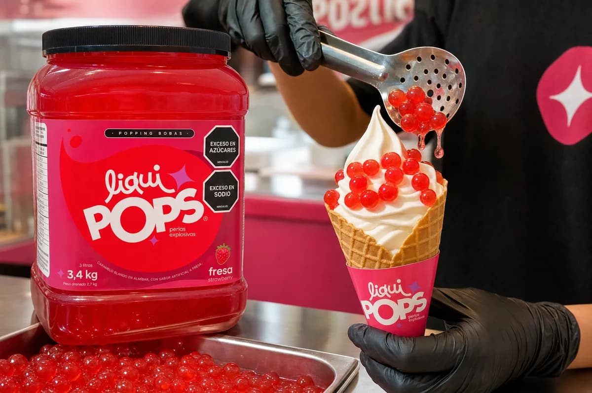 Cono de helado suave coronado con perlas explosivas LiquiPops rojas junto al tarro sabor fresa — preparación en heladería