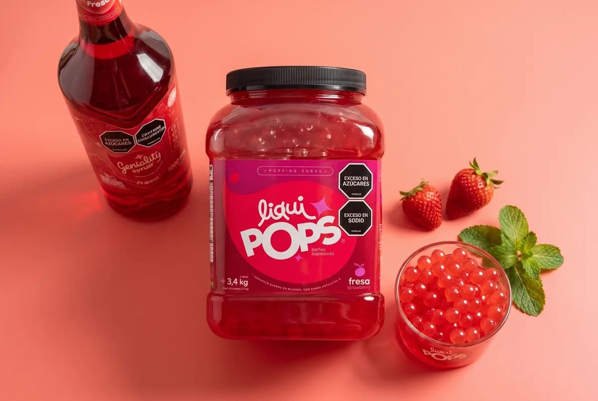 Tarro de 3,4 kg de perlas explosivas de fresa LiquiPops junto a sirope Geniality y fresas frescas — presentación mayorista