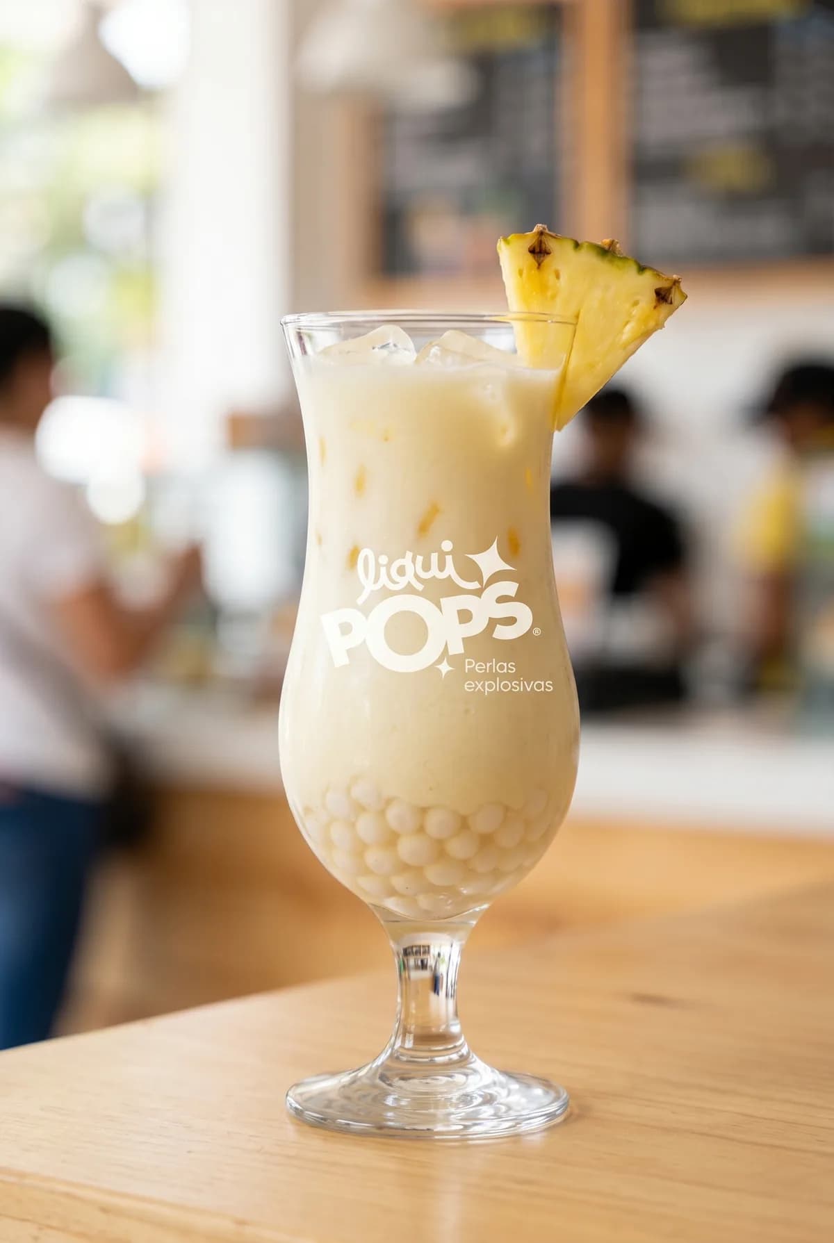 Piña colada cremosa de coco con perlas explosivas blancas LiquiPops y rodaja de piña — servida en cafetería luminosa