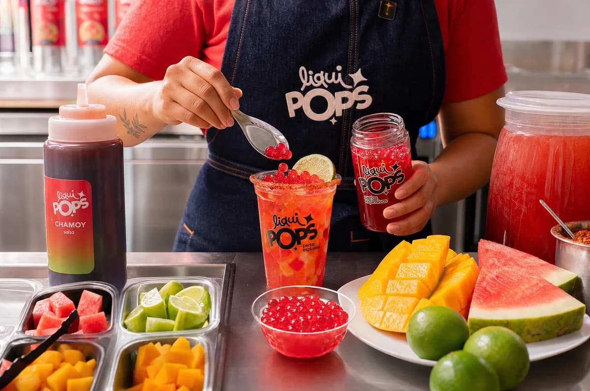 Persona sirviendo perlas explosivas rojas LiquiPops sobre una soda con frutas, chamoy, mango y sandía — barra de preparación