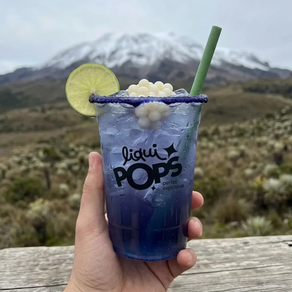 Soda azul violeta con perlas explosivas blancas LiquiPops y limon, sostenida frente a un nevado andino
