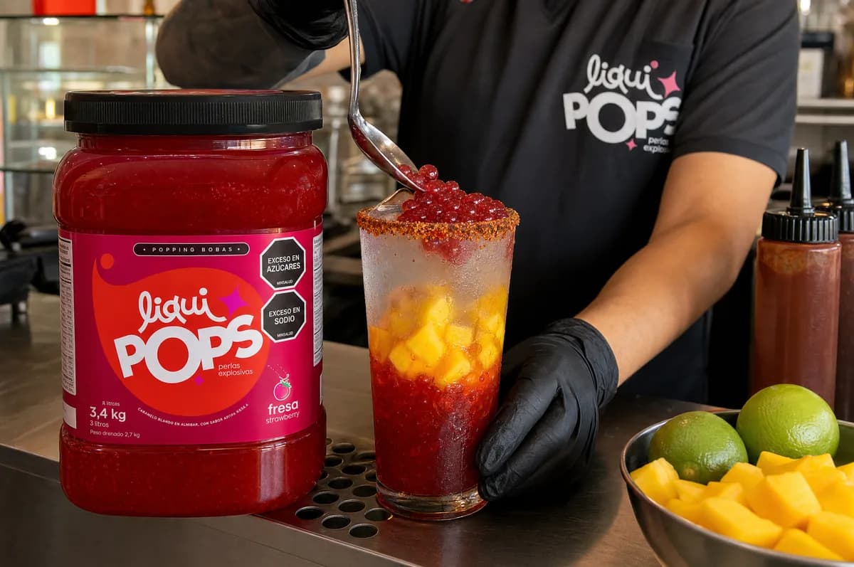 Barista sirviendo perlas explosivas de fresa LiquiPops sobre una soda loca con mango y chile, junto al frasco de 3,4 kg — preparación en barra