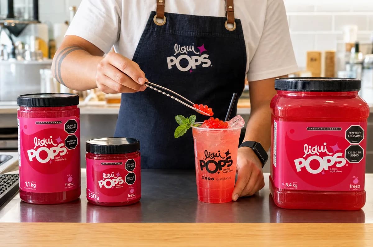 Barista sirviendo perlas explosivas LiquiPops sabor fresa sobre una soda loca, junto a tarros de 350 g, 1,1 kg y 3,4 kg