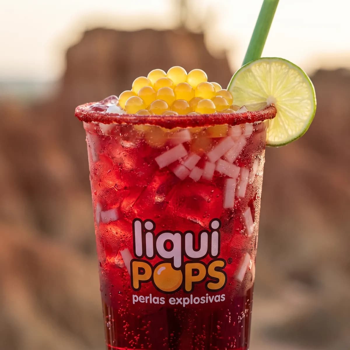 Soda loca de frutos rojos con perlas explosivas amarillas LiquiPops — borde de chamoy, limón y trozos de coco, primer plano con logo de marca