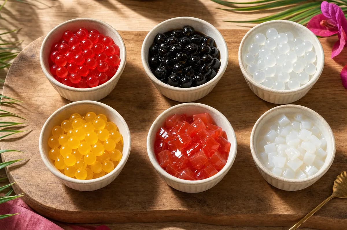 Tablero con seis bowls de toppings: perlas explosivas rojas y transparentes con perlas explosivas LiquiPops, tapioca negra y jelly de coco — surtido de coberturas para bubble tea