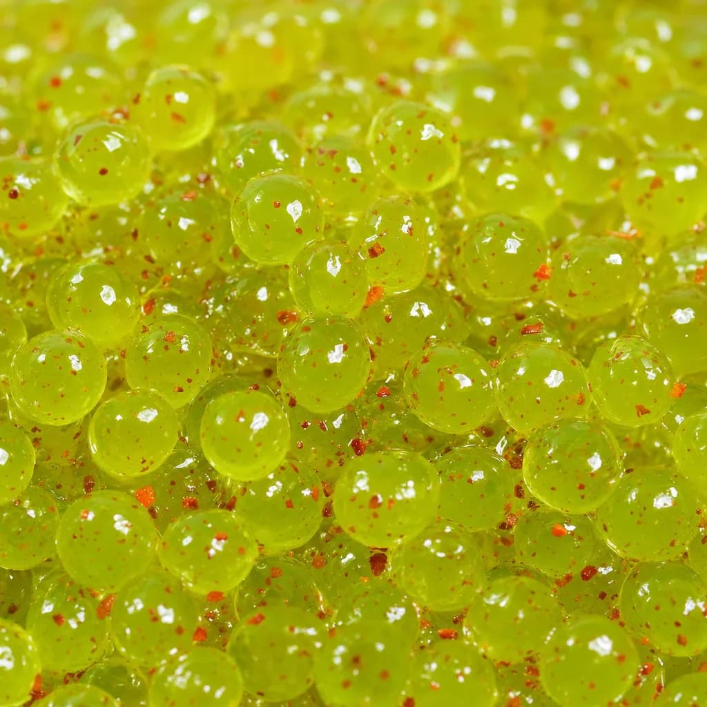Macro de perlas explosivas Maracululo Picante: esferas translúcidas amarillo verdoso con trocitos de chile rojos dentro del jugo