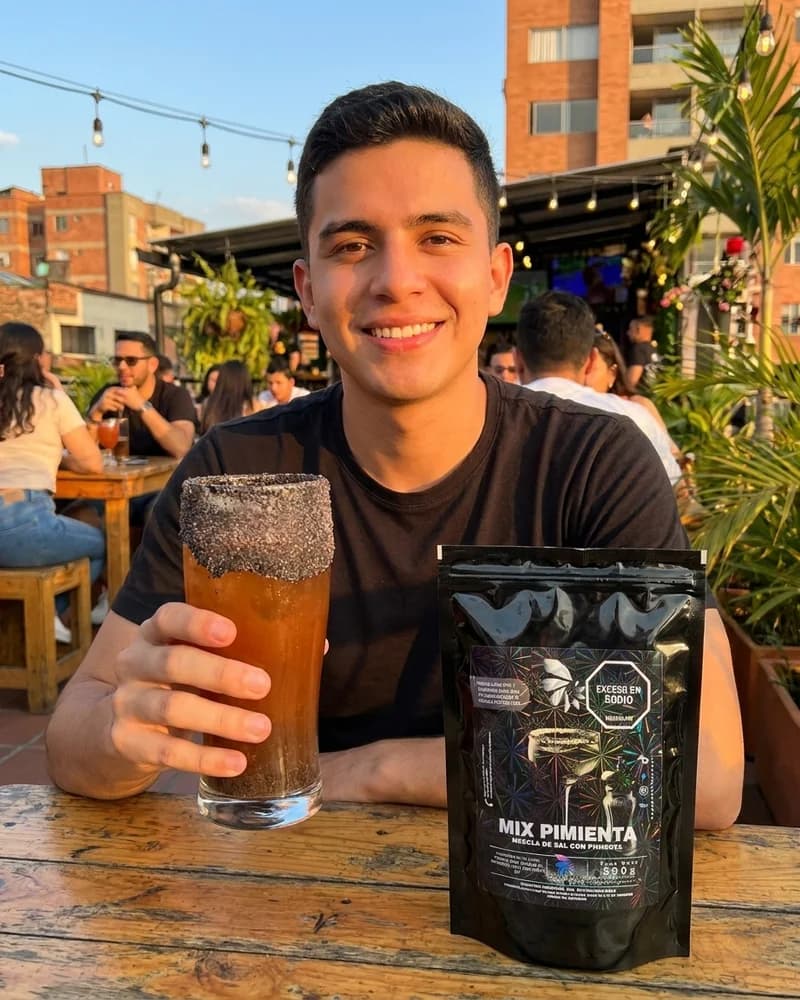 Hombre en bar al aire libre con vaso de michelada escarchada en pimienta y sal Skarcha con perlas explosivas LiquiPops junto al empaque mix pimienta by LiquiPOPS