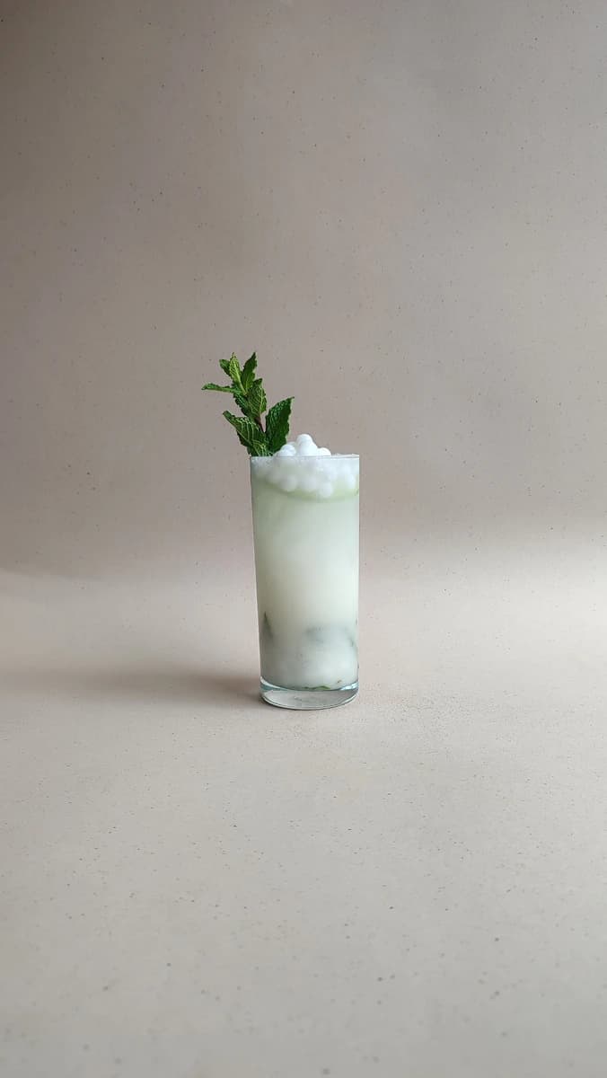 Cóctel mojito de coco con perlas explosivas LiquiPops y hierbabuena en vaso alto