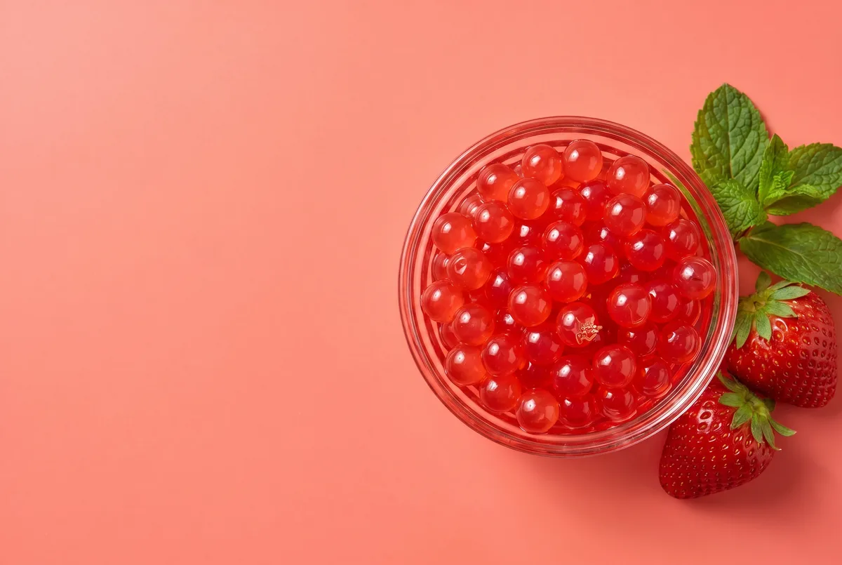 Bowl de perlas explosivas LiquiPops sabor fresa visto desde arriba con fresas frescas sobre fondo coral — topping rojo brillante