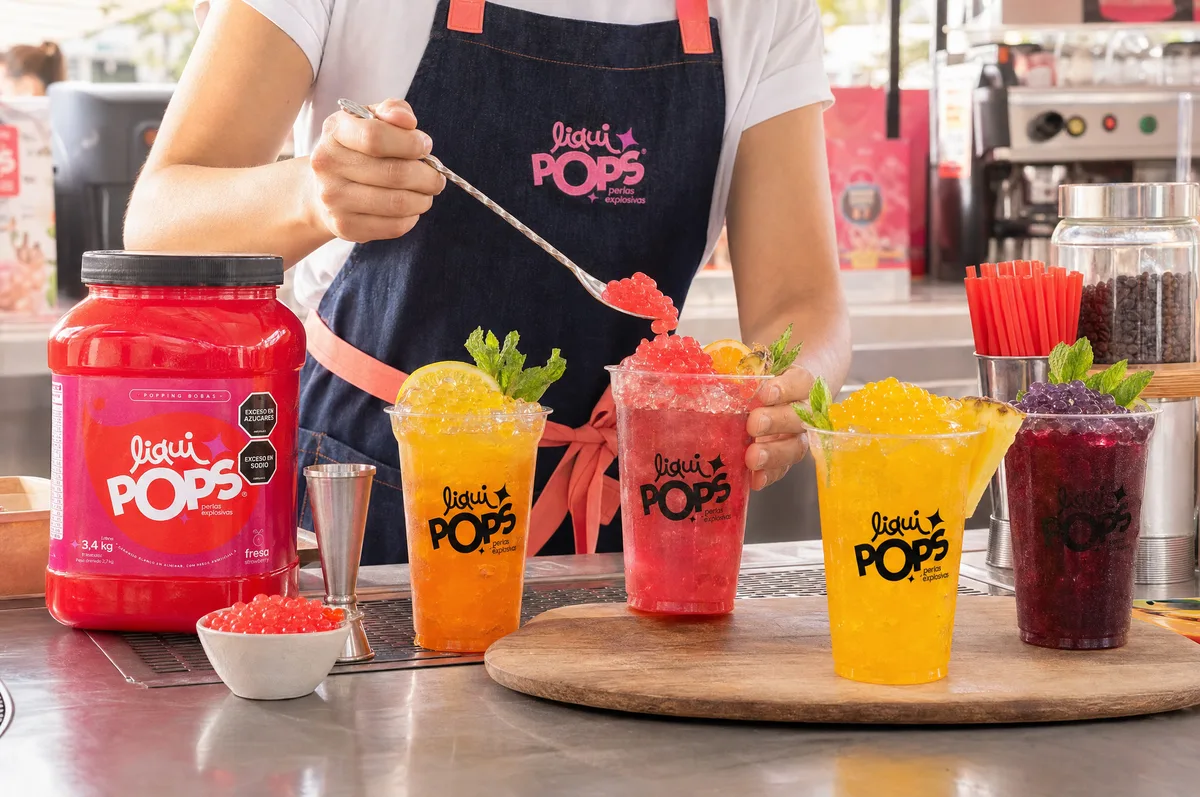 Barista sirviendo perlas explosivas LiquiPops sobre granizados surtidos de naranja, fresa, mango y mora azul en una barra
