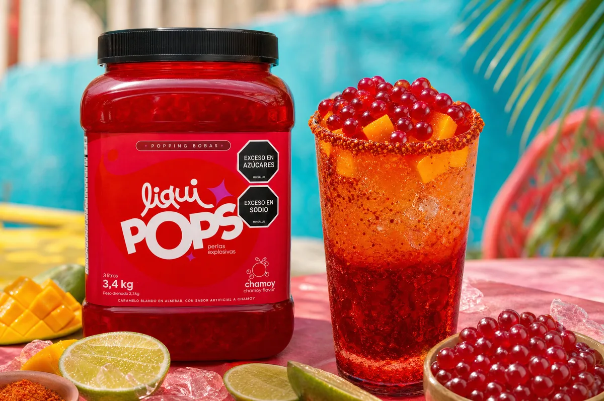 Michelada de chamoy con mango y perlas explosivas LiquiPops escarchada con chile, junto al frasco sabor chamoy — escena de piscina