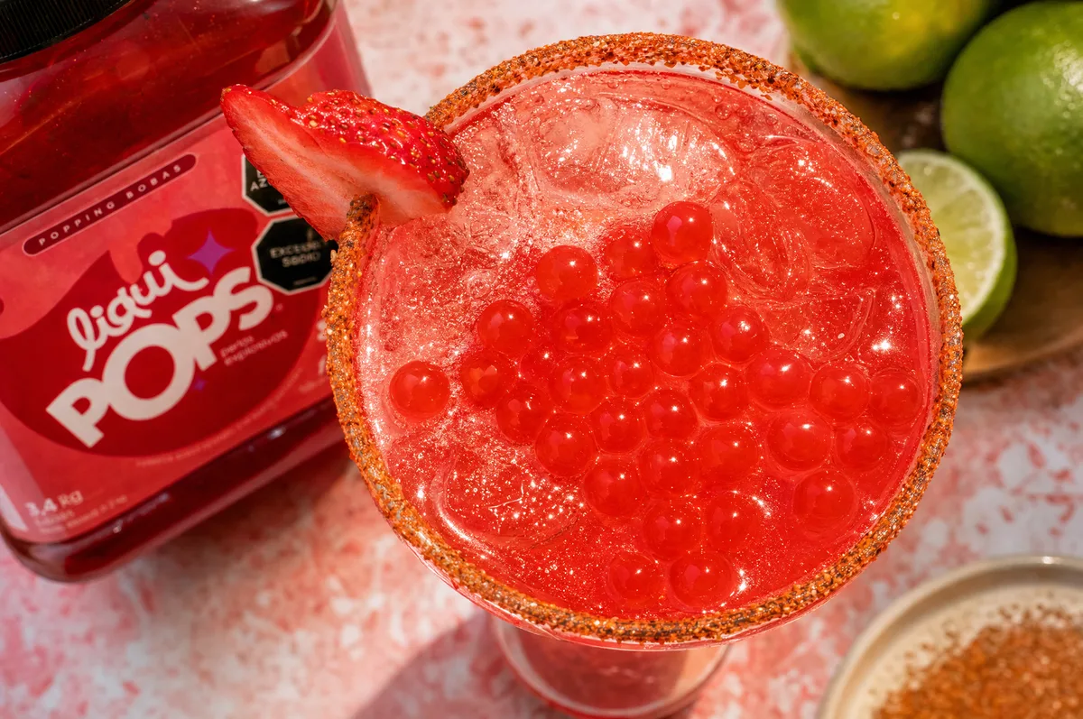 Perlas explosivas rojas sabor cereza LiquiPops sobre soda con escarcha y botella de sirope — bodegón con limones