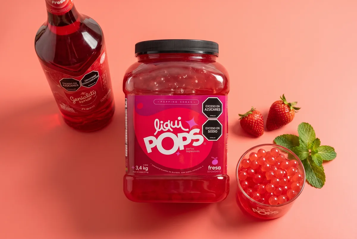 Tarro de 3,4 kg de perlas explosivas de fresa LiquiPops junto a sirope Geniality y fresas frescas — presentación mayorista