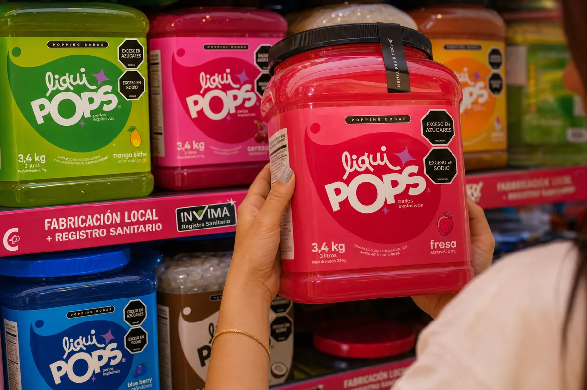 Mano sostiene un tarro de perlas explosivas LiquiPops sabor fresa frente a una gondola con varios sabores