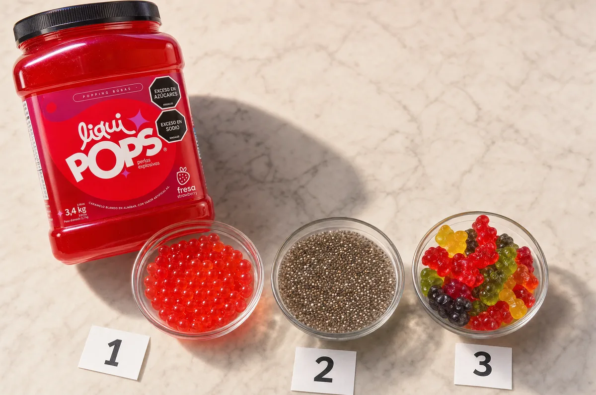 Tarro de perlas explosivas LiquiPops sabor fresa con cuencos de perlas rojas, chía y gomitas — comparativa de toppings sobre mármol
