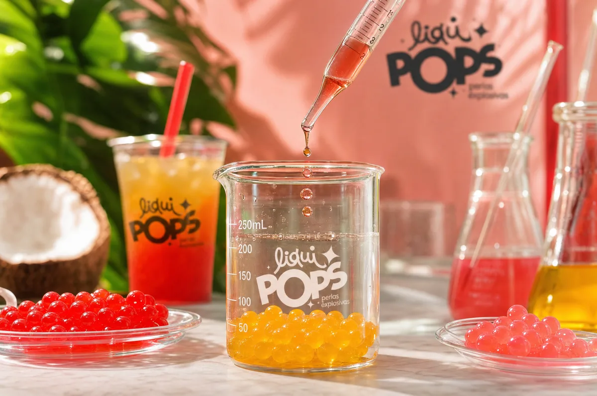 Perlas explosivas de mango en vaso de laboratorio LiquiPops con gotero, junto a perlas de fresa y coco — desarrollo de sabores
