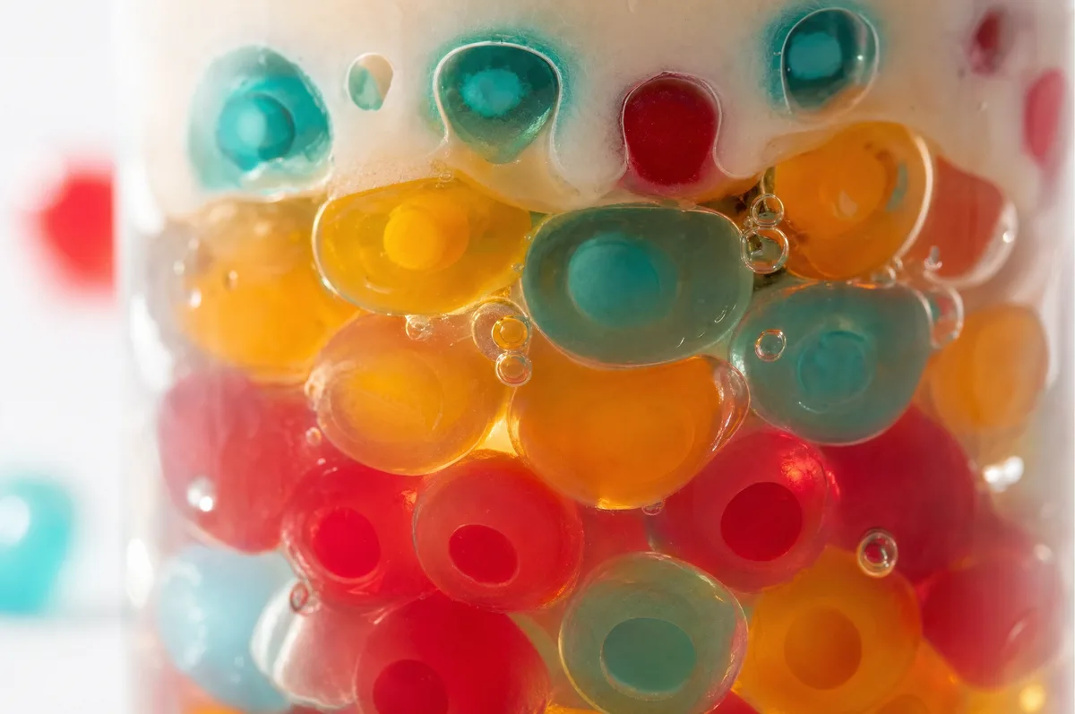 Primer plano macro de perlas explosivas multicolor LiquiPops dentro de un frasco — rojas, naranjas, amarillas y azules