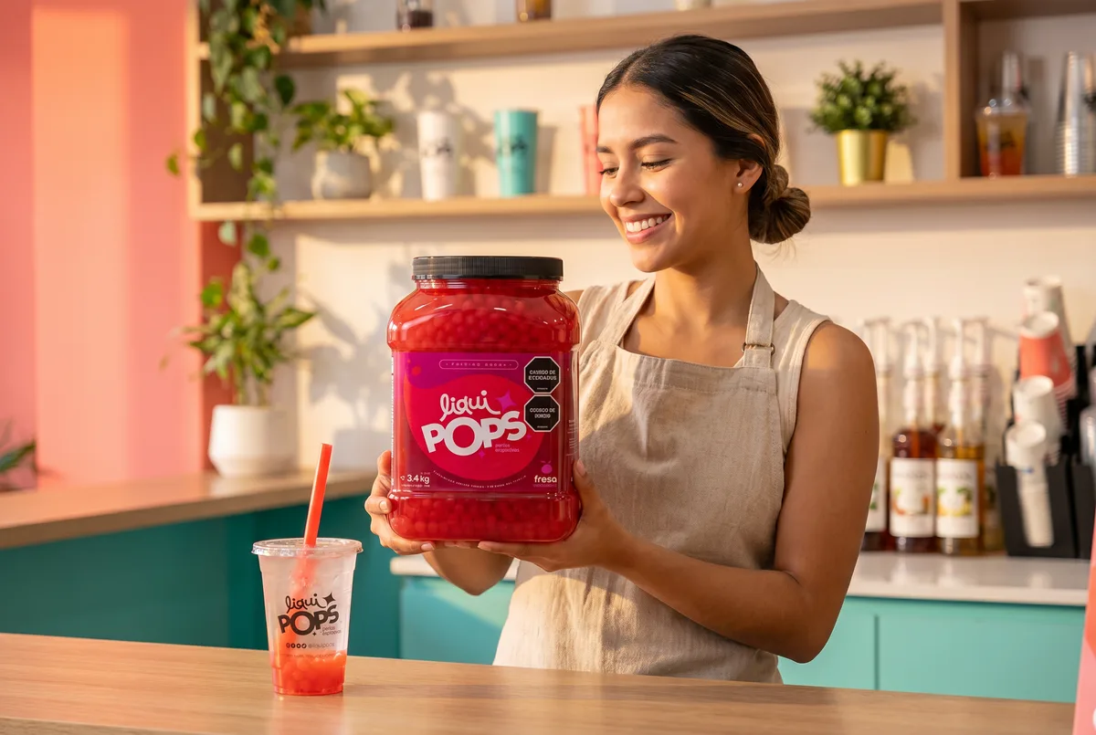 Barista sonríe sosteniendo un tarro de perlas explosivas de fresa LiquiPops junto a un vaso preparado — perlas explosivas LiquiPops para tu negocio