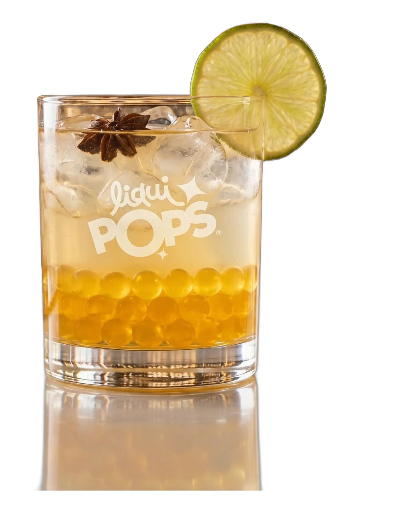 Cóctel de aguardiente con perlas explosivas amarillas LiquiPops, anís estrellado y rodaja de lima sobre fondo blanco