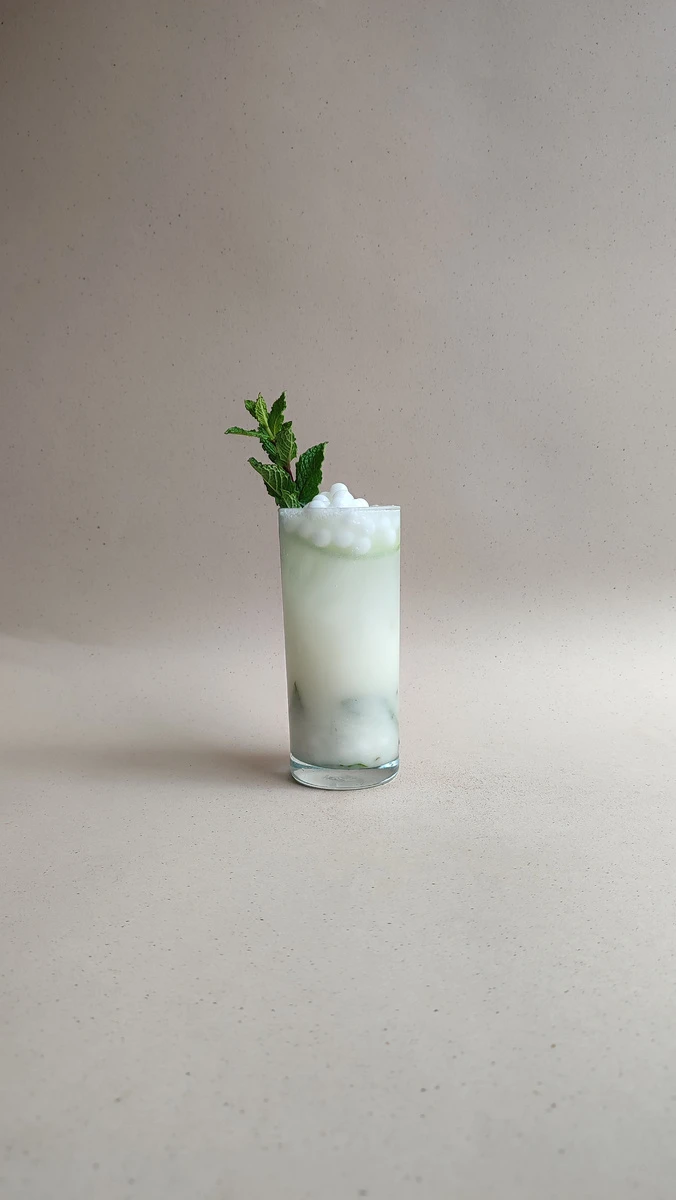 Cóctel mojito de coco con perlas explosivas LiquiPops y hierbabuena en vaso alto