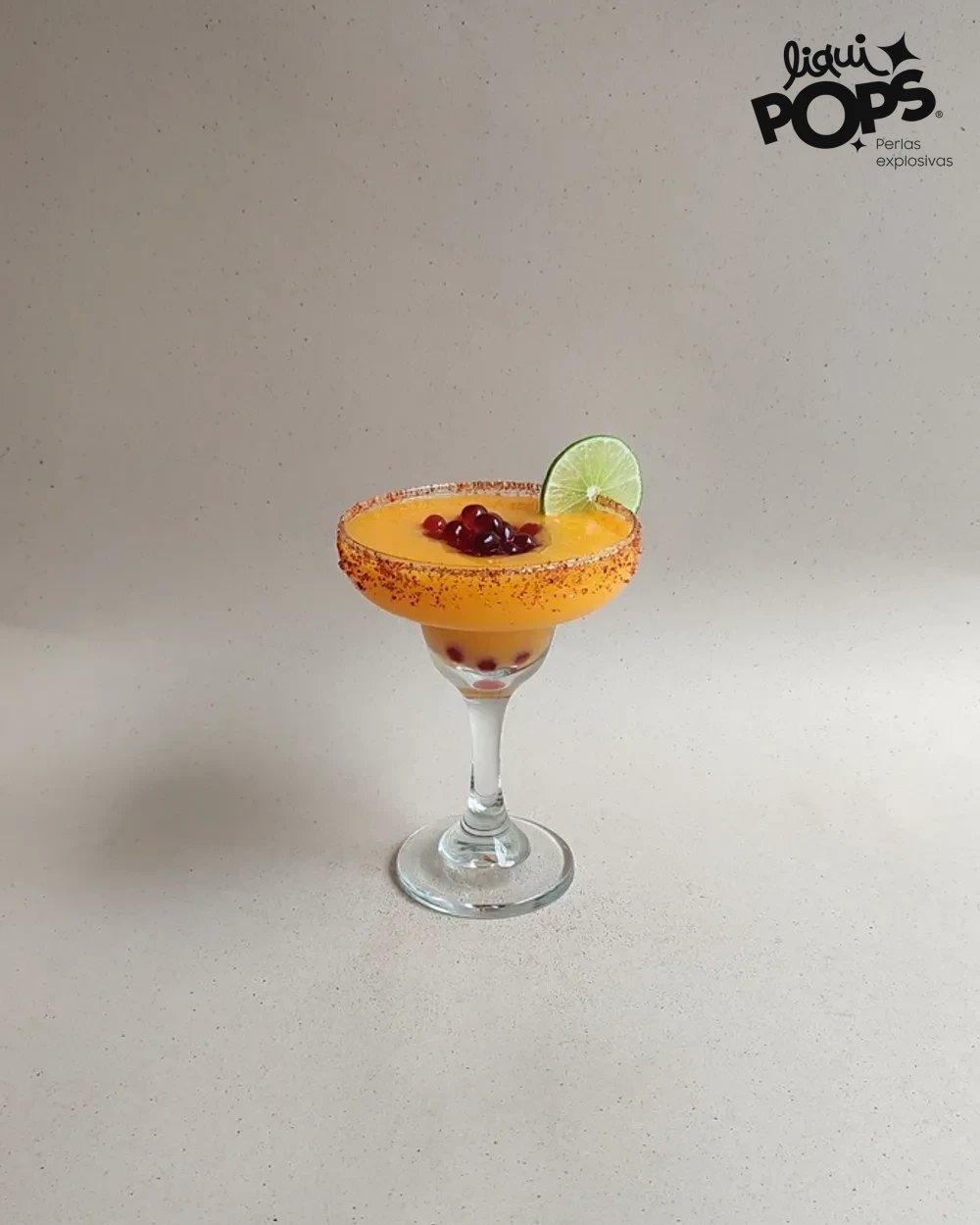 Margarita de mango con perlas explosivas LiquiPops y borde escarchado de chile servida en copa sobre mesa clara