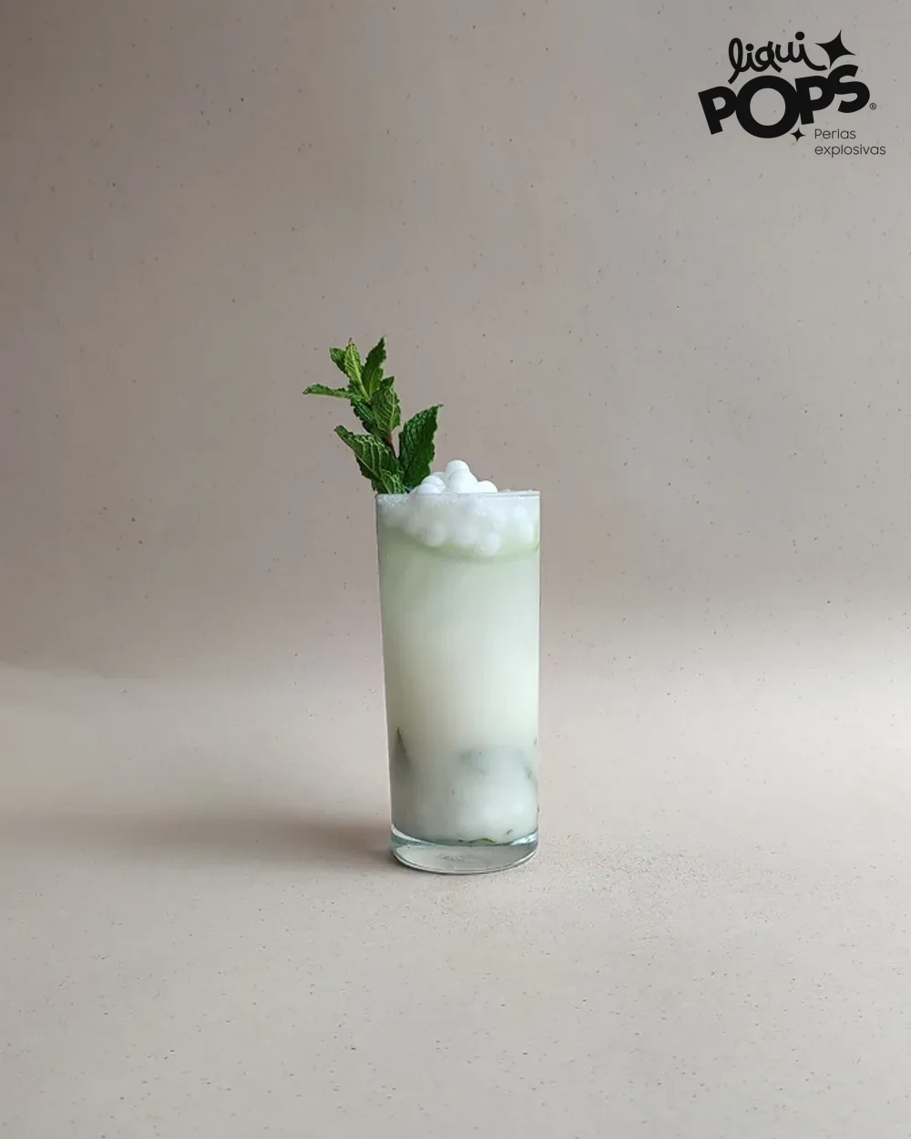 Mojito de coco con perlas explosivas LiquiPops y hierbabuena en vaso alto sobre fondo beige