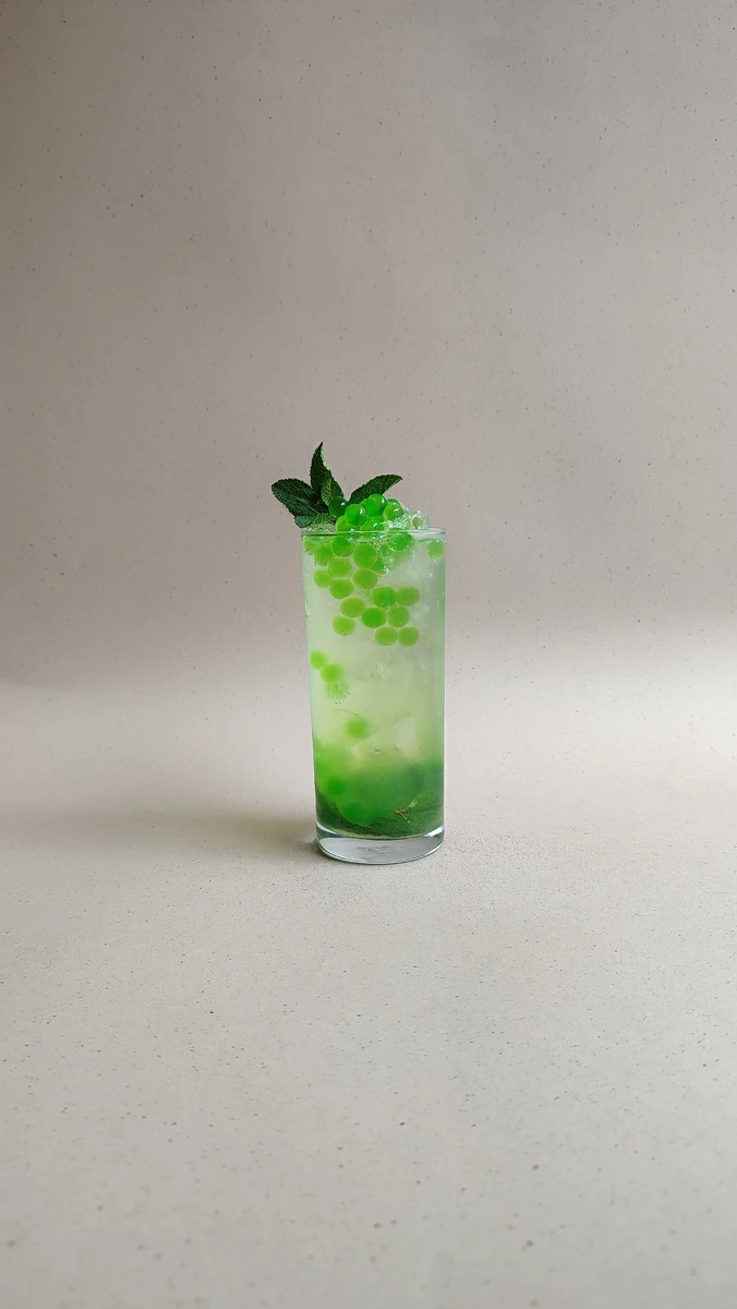 Soda de manzana verde con perlas explosivas verdes LiquiPops y hierbabuena sobre fondo beige